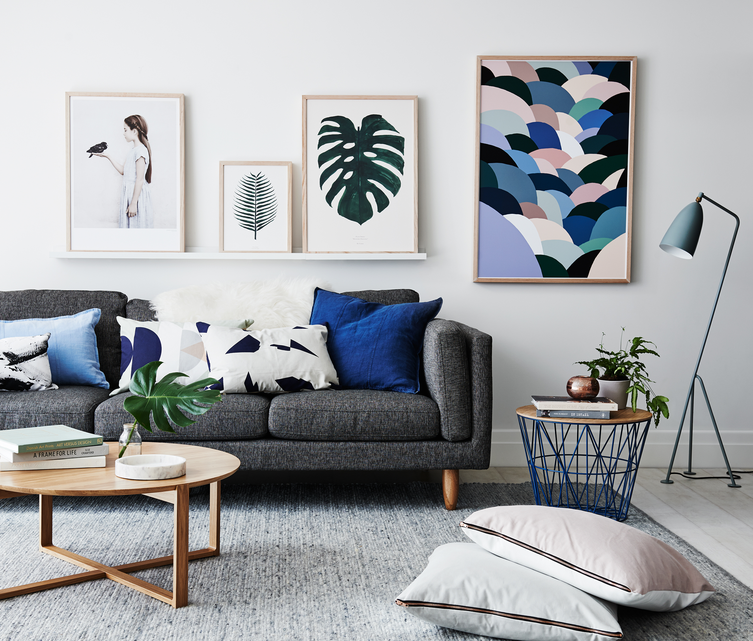 soggiorno con divano grigio e cuscini a fantasie blu, tappeto grigio, tavolino da caffè in legno chiaro e quadri a tema vario a parete